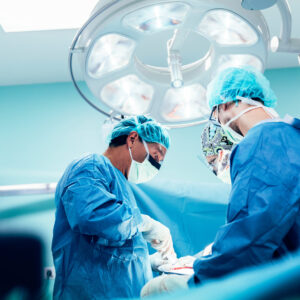 Schweineniere Mensch:Chirurgische Ärzte in blauer Schutzkleidung führen eine Operation durch, unter einem großen OP-Licht in einem Operationssaal."