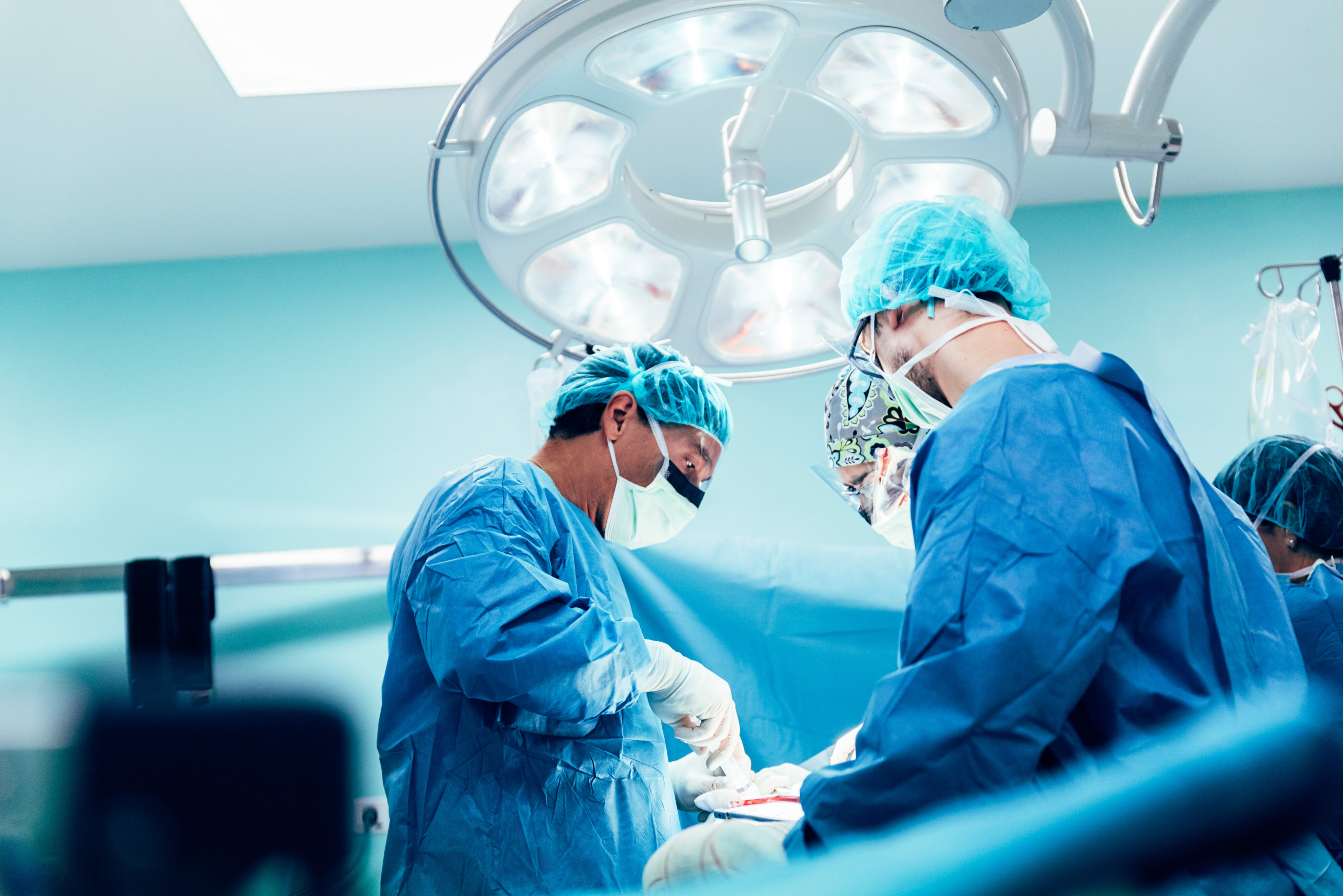 Schweineniere Mensch:Chirurgische Ärzte in blauer Schutzkleidung führen eine Operation durch, unter einem großen OP-Licht in einem Operationssaal."