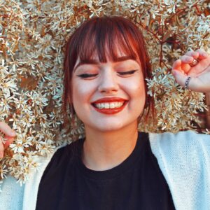 Parodontitis behandeln: Junge Frau mit rotem Lippenstift und geschlossenen Augen lächelt und liegt auf einer Blumenwiese