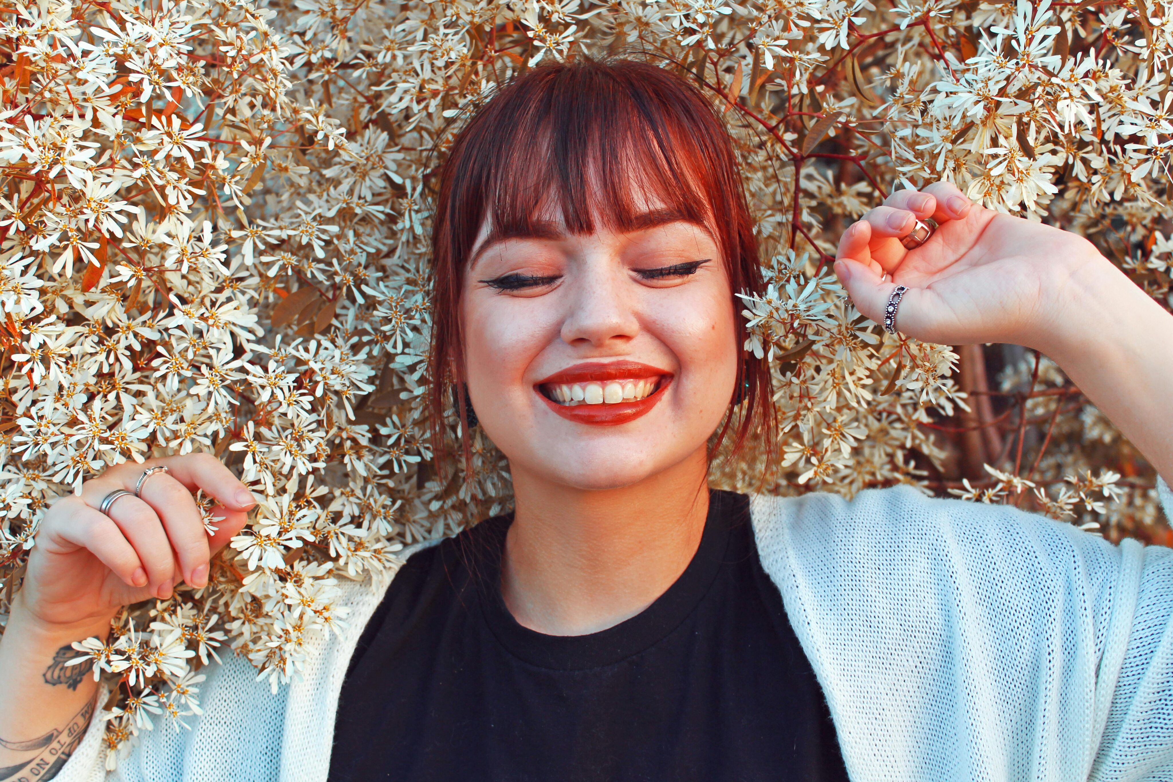 Parodontitis behandeln: Junge Frau mit rotem Lippenstift und geschlossenen Augen lächelt und liegt auf einer Blumenwiese